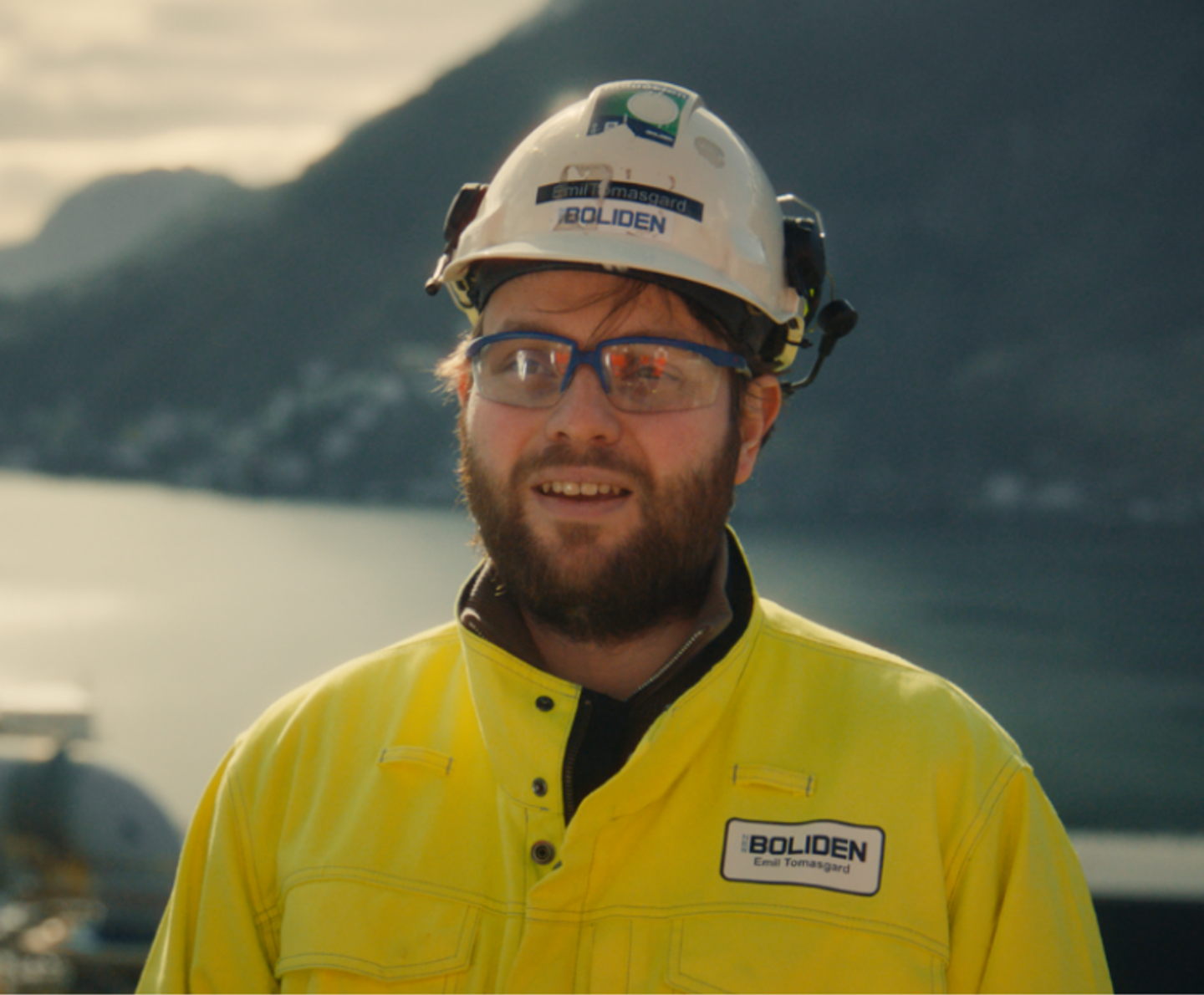 Man in protective gear with water and mountains in the background